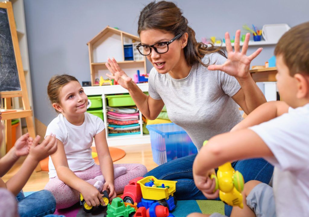Preschool teacher talking to group of children sitting on a floor at kindergarten