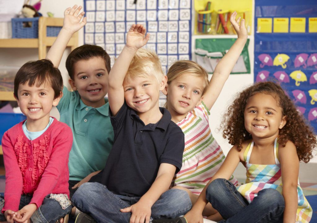 Group Of Elementary Age Schoolchildren Answering Question Sitting On Floor In Class